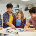 Diverse teenagers students group collaborating during a study session in classroom. Focused high school study group working together with books and notes while preparing for assignment. Girl and guy sharing ideas and helping each other in class at secondary school.